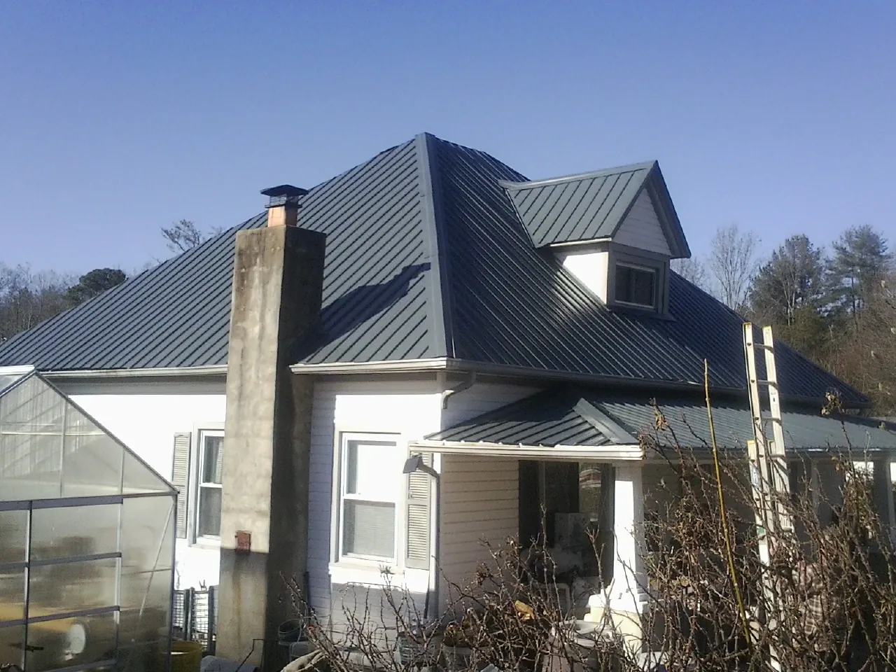 Dark blue standing seam metal roof on a white farmhouse with dormer — Slate & Tile Roof Repair by Roofing Brothers in Miller Place