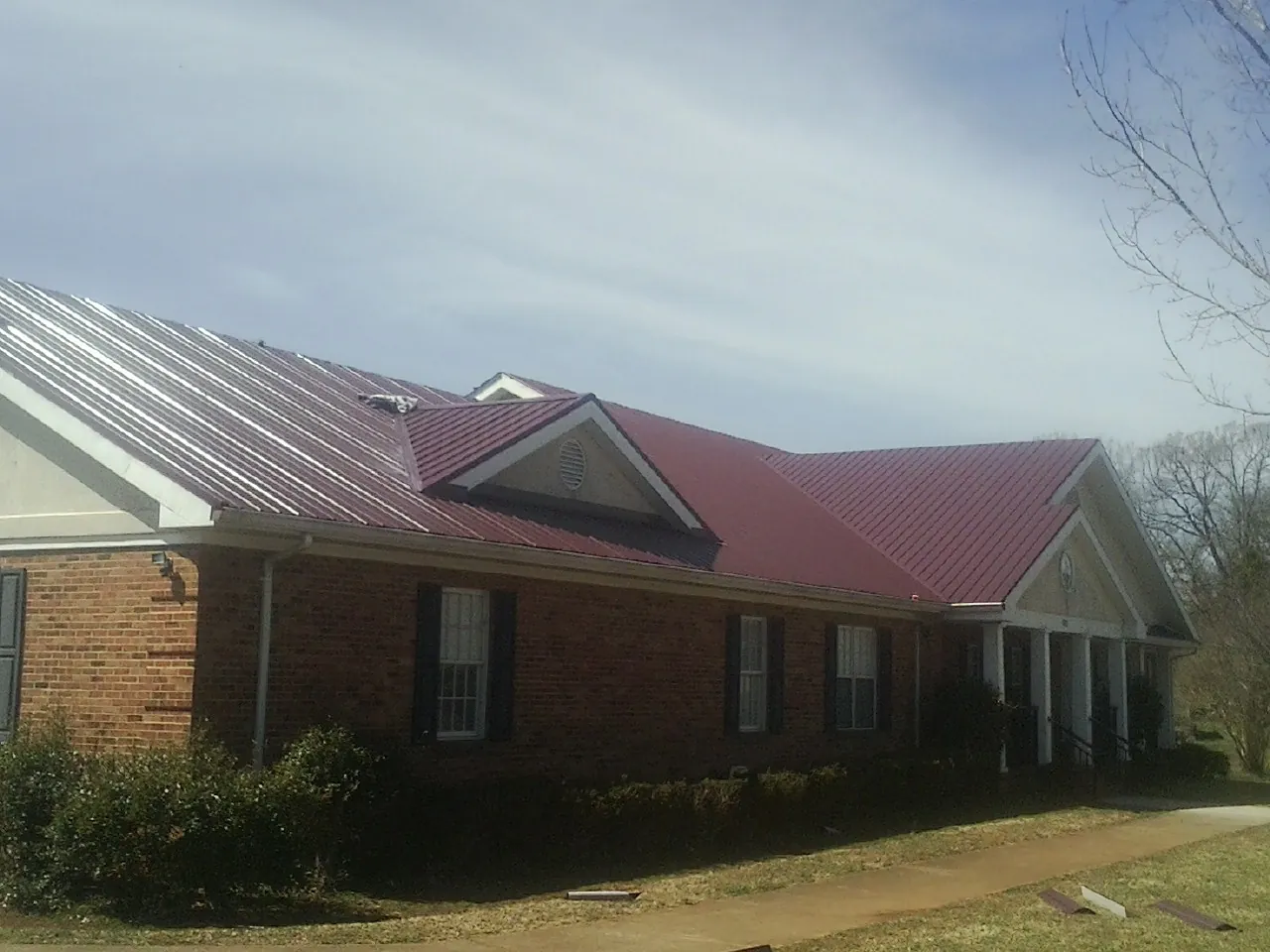 Red metal roof with gabled entries on a long brick building, from a Hail Damage Roof Repair job in Miller Place