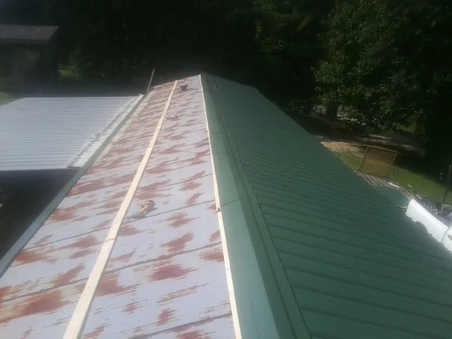 Old rusted panels beside newly installed green metal roofing — Wind Damage Roof Repair by Roofing Brothers in Miller Place