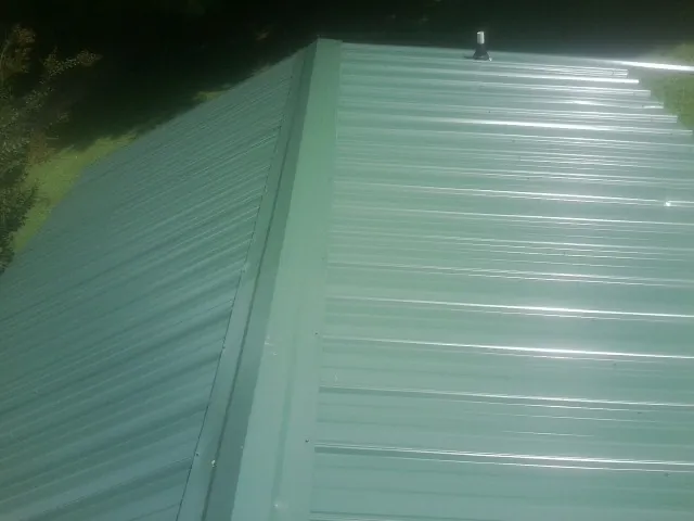 New green metal panels meeting at the ridge of a roof — Flat Roof Repair work by our crew in Miller Place