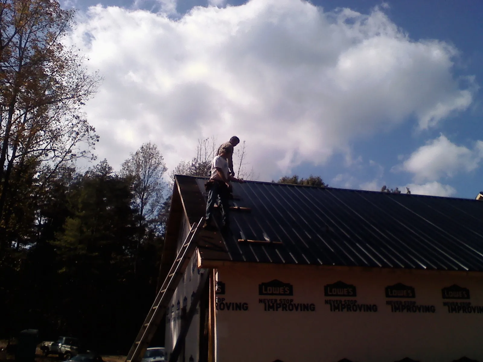 Roofer fastening dark metal panels high against a cloudy sky, from a Roof Inspection job in Miller Place
