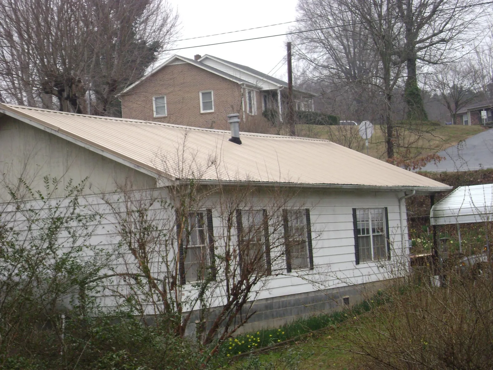 Tan metal roof on a white sided house set into a hillside — Commercial Roofing by Roofing Brothers in Miller Place