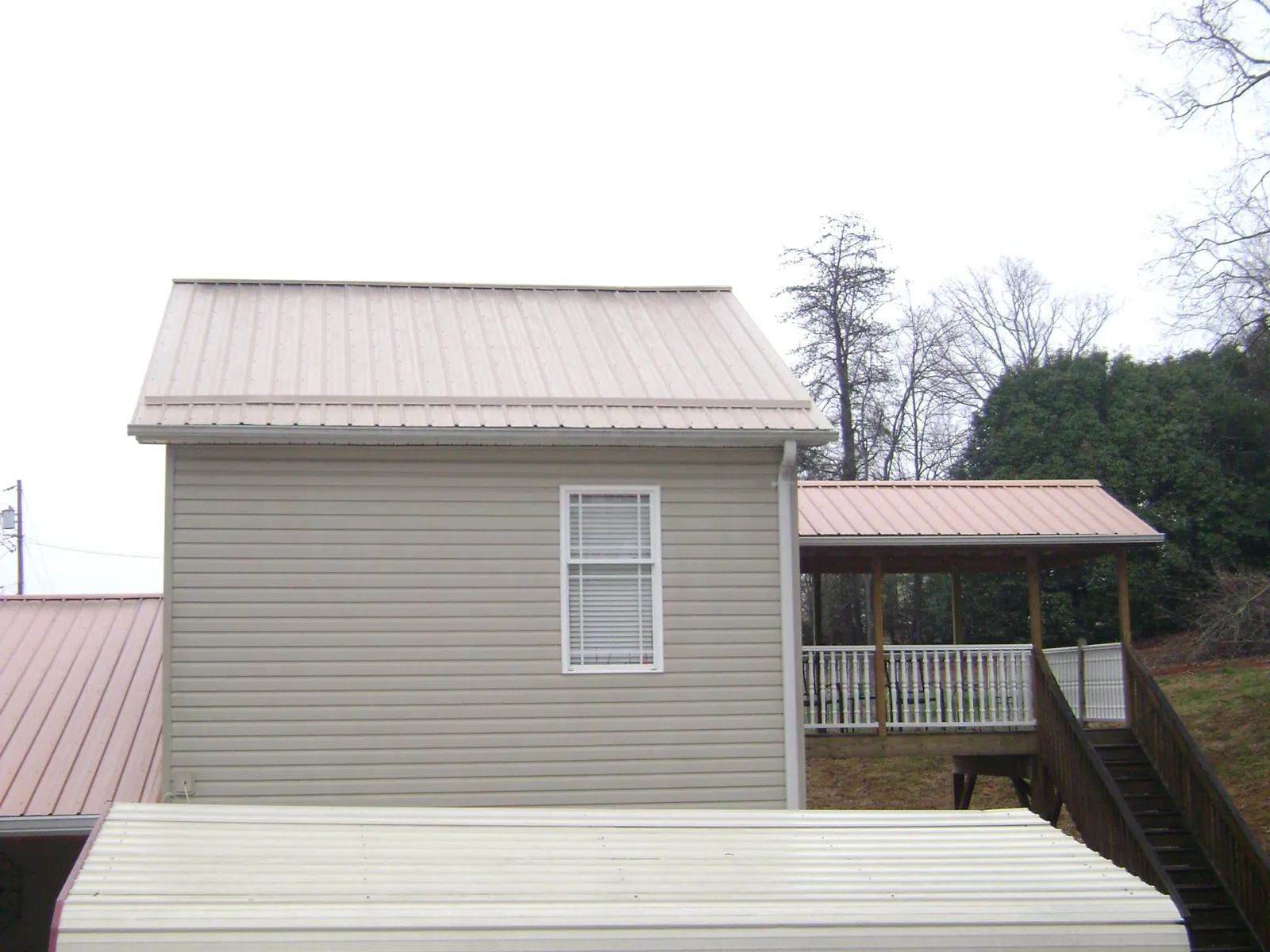 Tan metal roofs on a two story addition and attached porch, from a Roof Replacement job in Miller Place